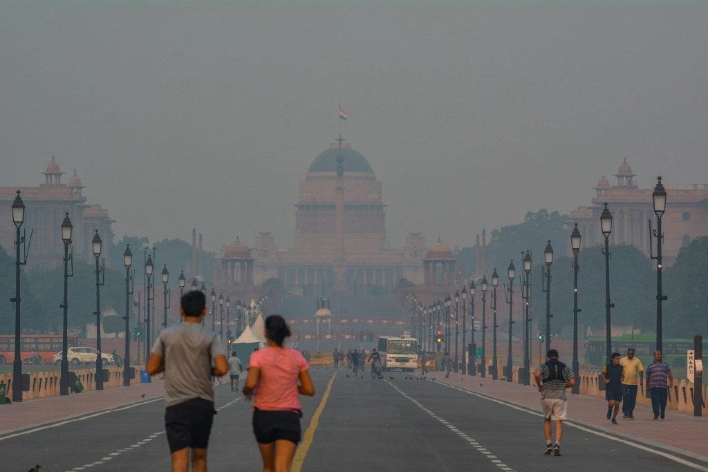 People jogging in smog near Rashtrapati Bhavan, New Delhi, highlighting urban pollution.